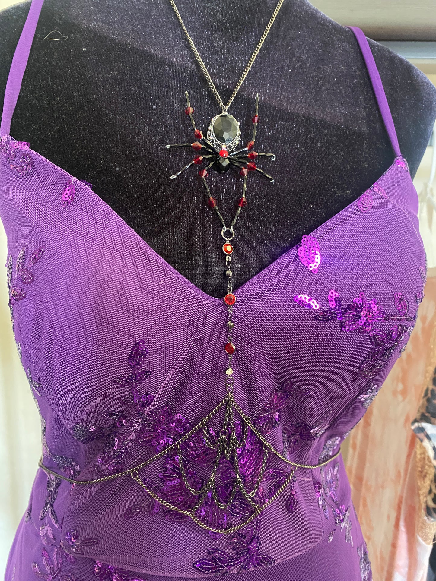 Purple embroidered dress with a spider necklace on a mannequin