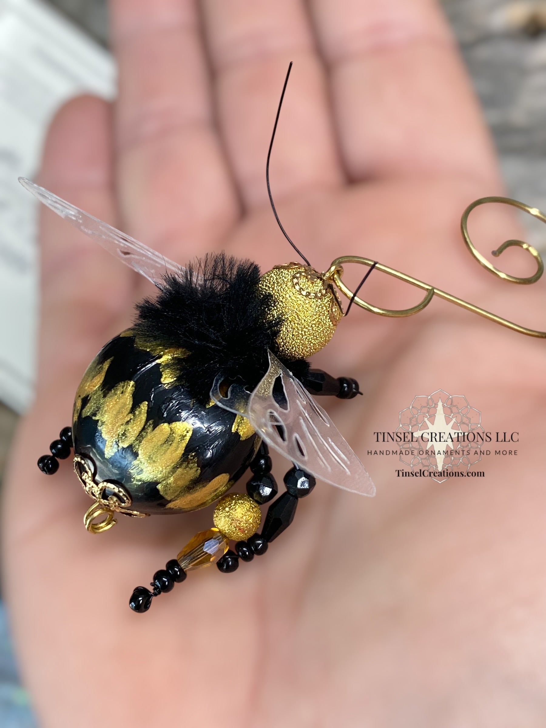 Decorative bee ornament with gold and black details held in a hand.