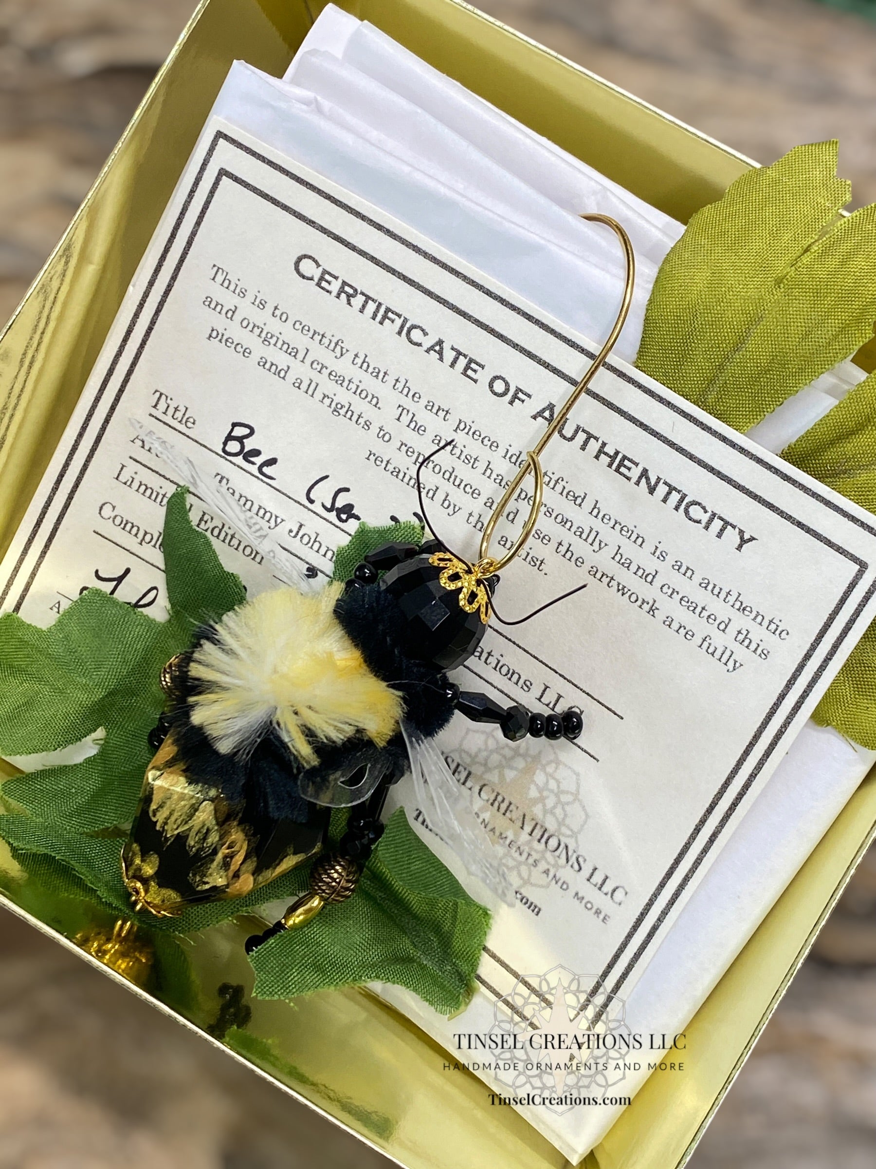Bee-shaped decorative item with a certificate of authenticity on green leaves.