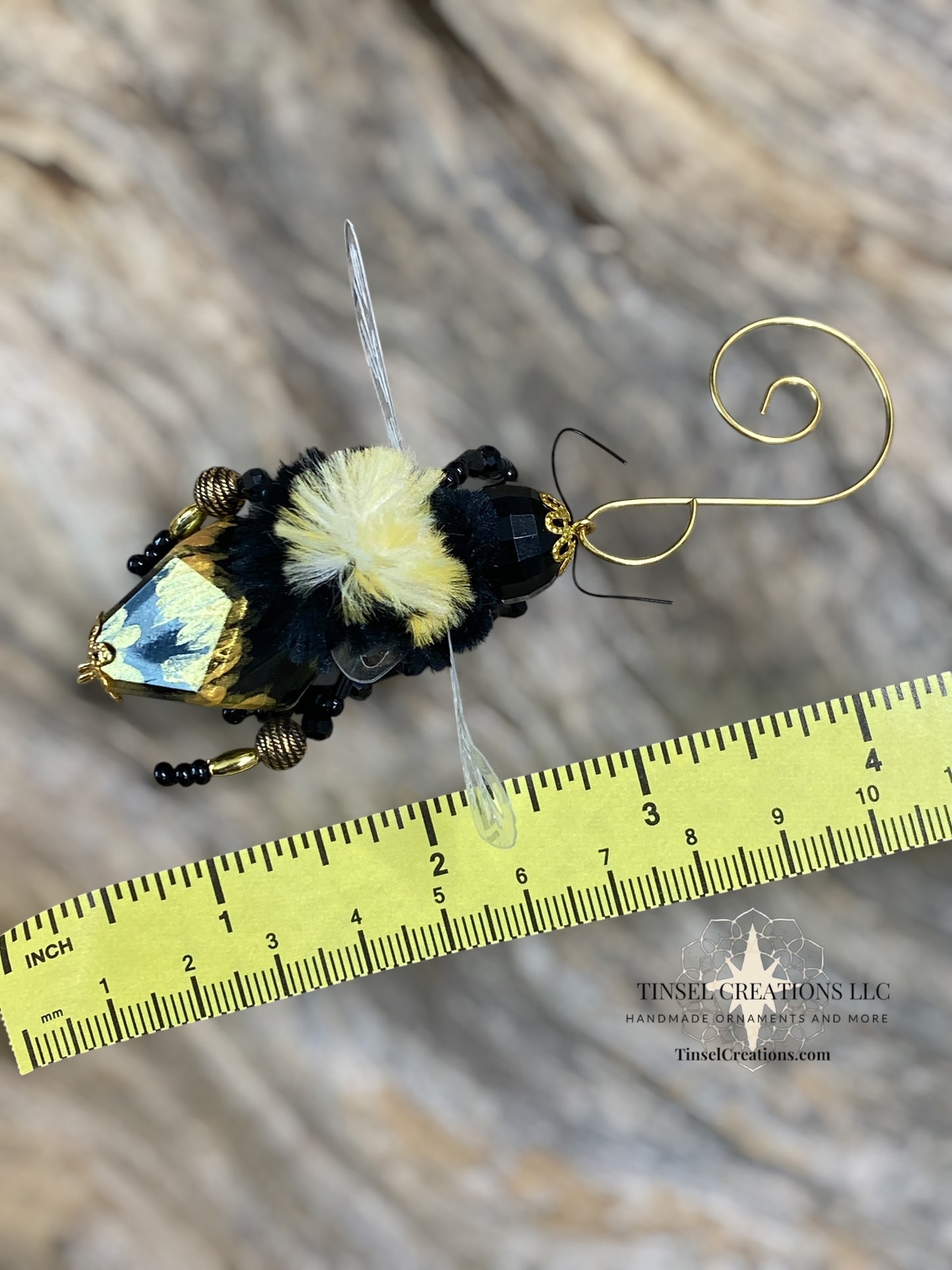 Handcrafted bee-shaped ornament with decorative elements on a wooden surface, measured against a ruler.