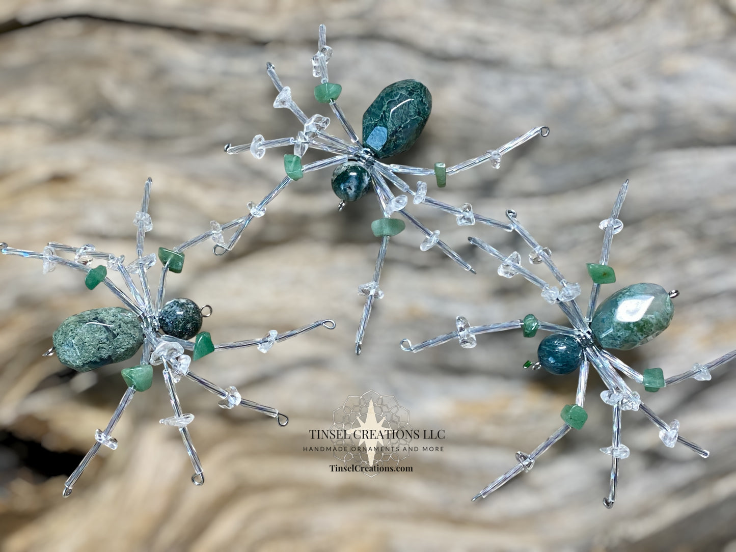 Decorative spider ornaments with green and clear stones on a textured surface