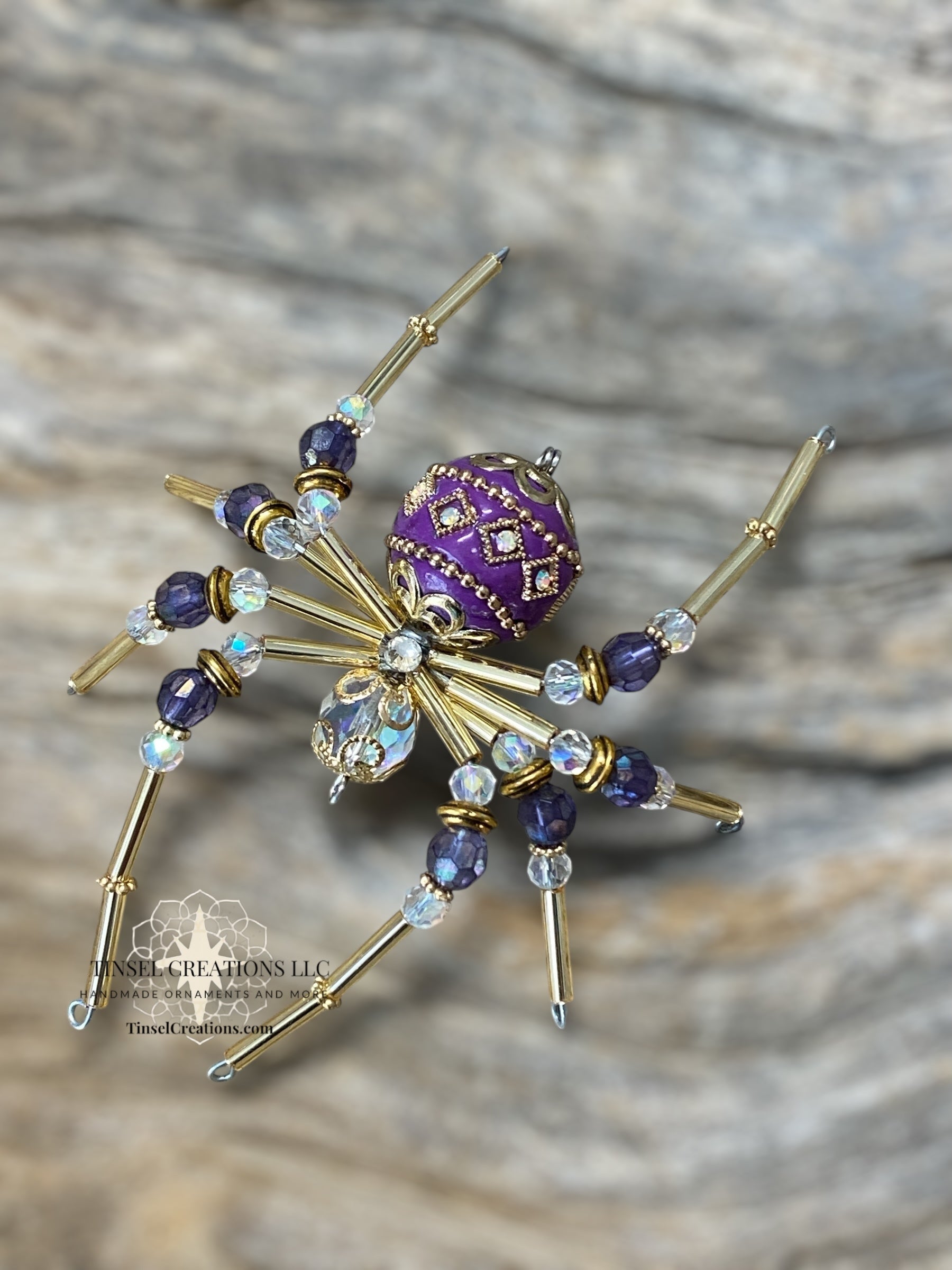 Decorative spider with purple center and gold legs on a textured surface