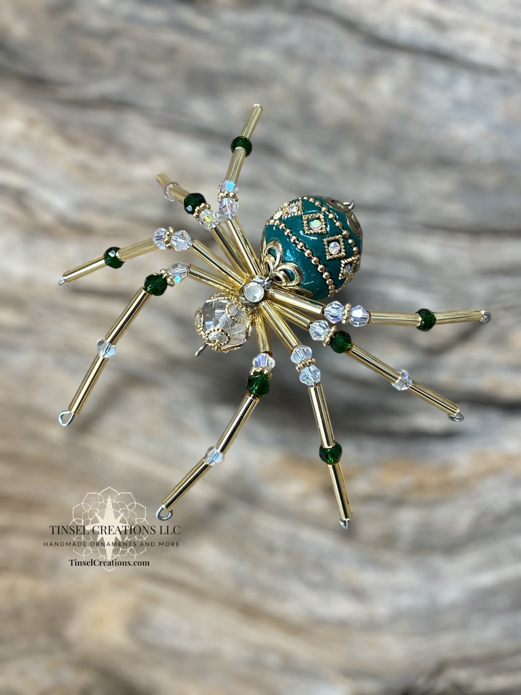 Decorative spider ornament with gold legs, green and clear gemstones on a textured surface.