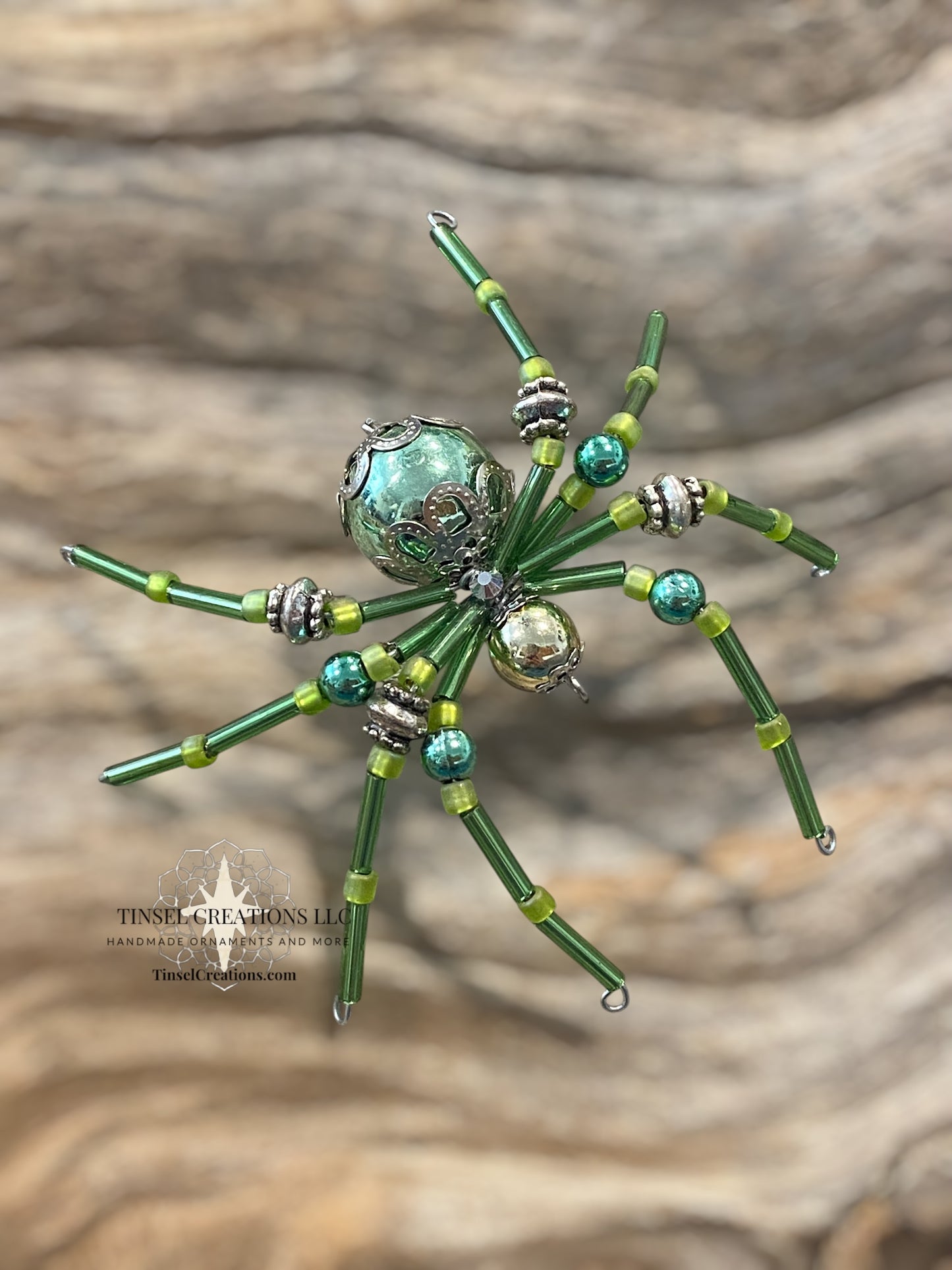 Spider-shaped ornament with green and silver beads on a wooden background